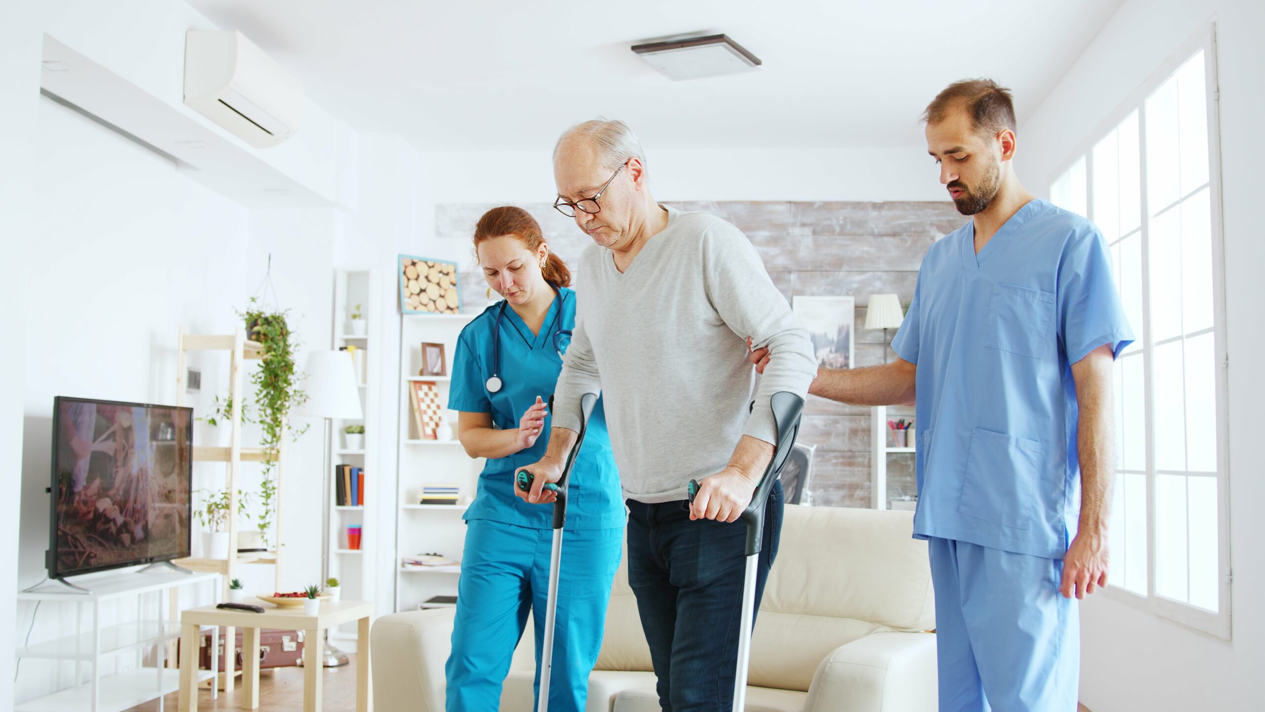 equipe-d-infirmieres-ou-de-travailleurs-sociaux-aidant-un-vieil-homme-handicape-a-sortir-avec-ses-bequilles-de-la-chambre-de-la-maison-de-retraite